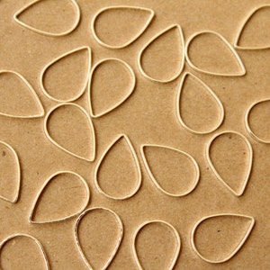 Puede incluir: Primer plano de un grupo de dijes de metal plateado en forma de lágrima sobre una superficie marrón.