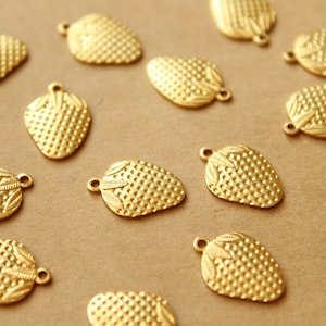May include: A collection of gold-toned metal charms shaped like strawberries. Each charm has a textured surface and detailed leaf accents.