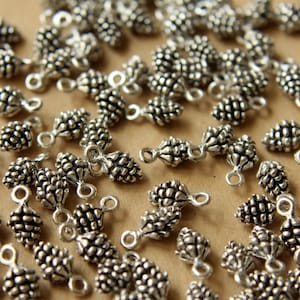 Könnte beinhalten: Eine große Menge an silberfarbenen Metall-Kiefernzapfen-Anhängern mit einer Öse zum Anbringen an Schmuck oder anderen Bastelarbeiten.
