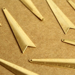 Può includere: Un gruppo di ciondoli a forma di freccia in metallo dorato con una punta appuntita e un piccolo foro in alto.