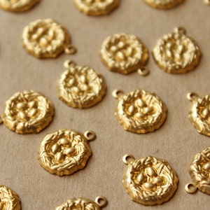May include: A collection of gold-toned metal charms shaped like bird nests with small, round, raised details resembling eggs. Each charm has a loop for attaching to a necklace or bracelet.