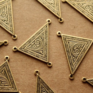 Peut inclure: Un groupe de breloques triangulaires en métal doré ornées de motifs floraux complexes. Chaque breloque a trois trous pour l'attacher à des bijoux ou d'autres objets artisanaux.