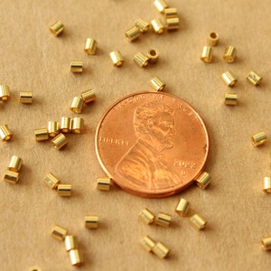 May include: A close-up of a pile of gold jump rings next to a US penny. The penny is dated 2022. The jump rings are small and are used for jewelry making.