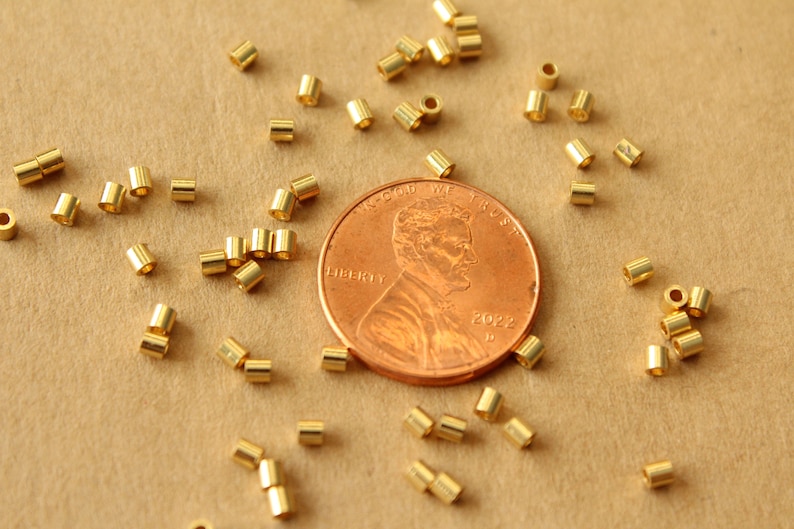 May include: A close-up of a pile of gold jump rings next to a US penny. The penny is dated 2022. The jump rings are small and are used for jewelry making.
