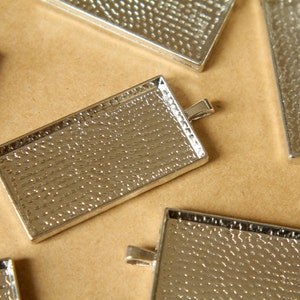 May include: Five silver metal rectangular trays with a textured surface and a loop for hanging. The trays are arranged on a brown surface.