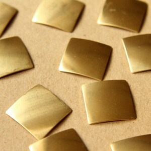 May include: A collection of small, square, brass tiles arranged on a brown surface. The tiles are smooth and shiny, reflecting light.