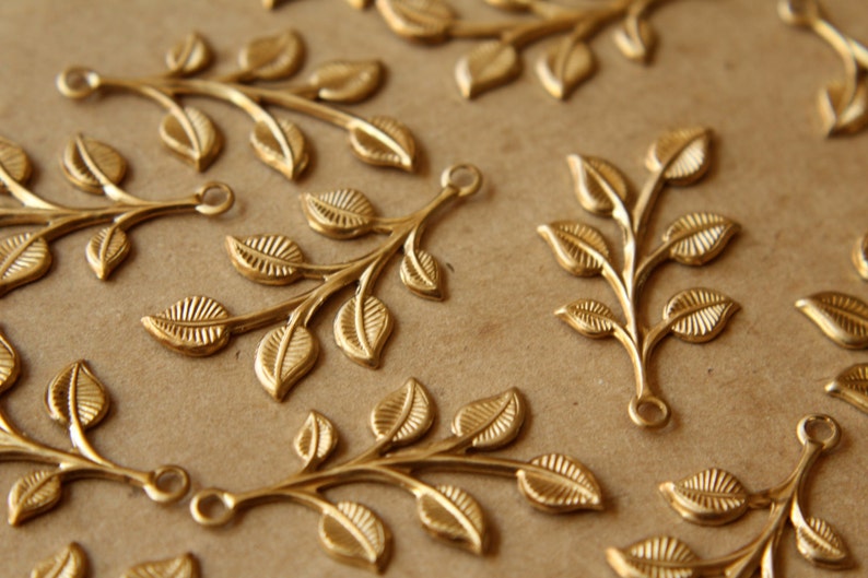 May include: A collection of gold-toned metal leaf branch charms with a loop at the top for attaching to jewelry or other crafts.