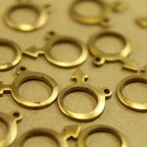 May include: A collection of gold-toned metal charms in the shape of a circle with an arrow pointing to the right. The charms are arranged on a brown surface.