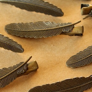 May include: A set of six antique gold-toned feather hair clips. The clips are made of metal and have a detailed feather design.