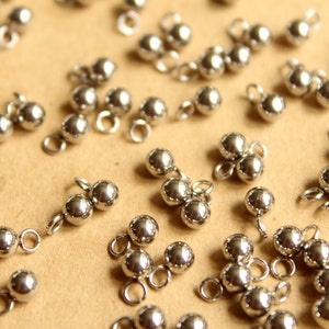 May include: A collection of silver metal beads with loops, some are single beads and others are connected in groups of two or three.