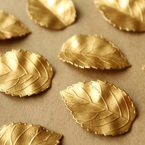 May include: A collection of ten gold leaf-shaped decorative items with a textured surface. The leaves are arranged on a brown background.
