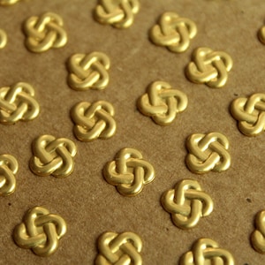 May include: A sheet of gold-colored metal decorative embellishments in the shape of a four-leaf clover knot. The embellishments are arranged in a repeating pattern on a brown surface.