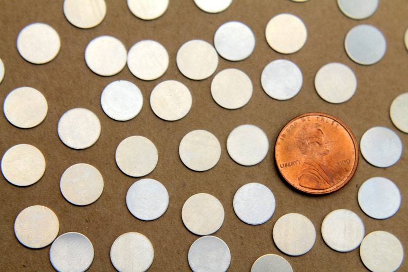 May include: A close-up of a pile of silver-colored round confetti, with a US penny coin in the center. The confetti is scattered on a brown surface.