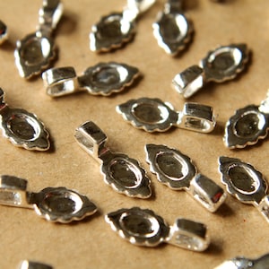 May include: A group of silver-toned metal pendant clasps with a teardrop shape. The clasps have a small loop at the top for attaching to a chain or cord.