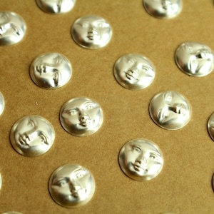 May include: A sheet of brown paper with multiple silver-colored round buttons featuring a face design. Each button has a different facial expression.