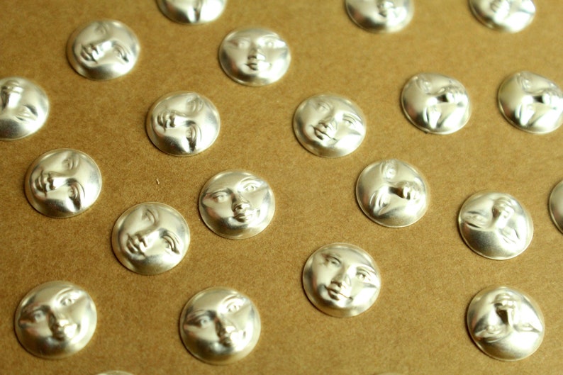 May include: A sheet of brown paper with multiple silver-colored round buttons featuring a face design. Each button has a different facial expression.