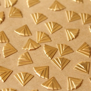 May include: A collection of gold-colored metal decorative pieces in the shape of a fan. The pieces are arranged in a repeating pattern on a brown surface.