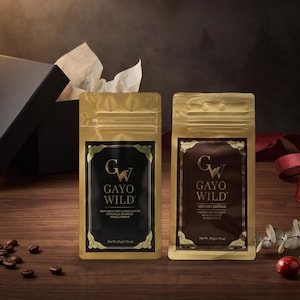 Könnte beinhalten: Zwei goldfarbene Kaffeebeutel mit der Aufschrift Gayo Wild. Der linke Beutel hat ein schwarzes Etikett, der rechte ein dunkelbraunes Etikett mit dem Text Vintage Edition. Jeder Beutel zeigt unten ein Nettogewicht von 50g (1,76 oz) an.