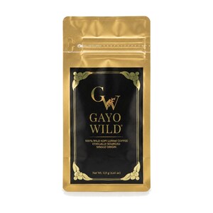 Puede incluir: Una bolsa de café dorada con una etiqueta rectangular negra que presenta el texto GAYO WILD, 100% WILD KOPI LUAK COFFEE, ETHICALLY SOURCED, SINGLE ORIGIN y Net Wt. 125 g, con detalles decorativos de hojas doradas en las esquinas.