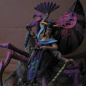 May include: A painted miniature figurine featuring a hybrid creature with a human upper body and a large purple spider-like lower body. The figure wears a blue and purple outfit, holds a folding fan, and wields a long, bladed weapon with gear details.