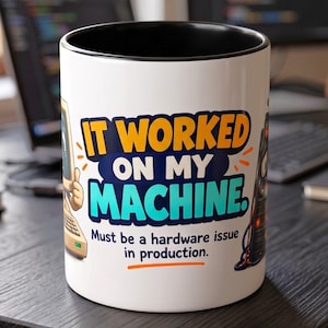 May include: A white ceramic mug with a black interior featuring a graphic of a vintage computer and the text IT WORKED ON MY MACHINE. Must be a hardware issue in production. The design includes orange and teal lettering on the front.
