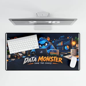 May include: A rectangular desk mat featuring a blue monster character working at a computer with charts and graphs. The text reads DATA MONSTER TAME THE CHAOS. A white keyboard and mouse are placed on the mat, which sits below a computer monitor.