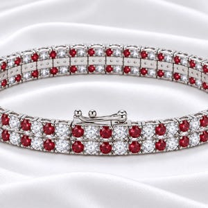Könnte beinhalten: Ein zweireihiges Tennisarmband mit abwechselnd rund geschliffenen roten Rubinen und klaren weißen Steinen in einem silberfarbenen Metallband. Das Armband verfügt über einen sicheren Kastenschloss-Verschluss mit Sicherheitsbügel.
