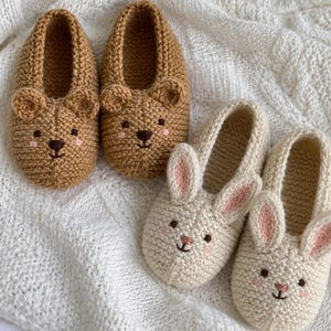 May include: Two pairs of hand-knitted slippers. One pair is tan with round bear ears, a dark brown nose, and pink cheeks. The other pair is cream with long rabbit ears featuring pink inner details, a small pink nose, and pink cheeks.