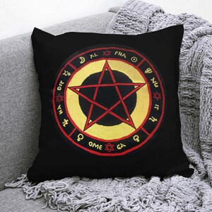 Può includere: Un cuscino quadrato nero con un design centrale raffigurante un pentagramma rosso all'interno di un cerchio dorato. Il bordo rosso esterno presenta la scritta ALPHA e OMEGA, insieme a vari simboli planetari e piccole icone a stella.