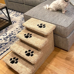 May include: Beige pet stairs with four steps and black paw prints on each step. The stairs are in front of a gray couch.