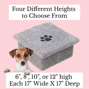 May include: A gray, square, plush pet step with a black paw print on top. Text reads: Four Different Heights to Choose From, 6", 8", 10", or 12" high, Each 17" Wide X 17" Deep. A small brown and white dog is positioned in the lower left corner.