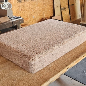 Puede incluir: Una plataforma rectangular cubierta con un material de alfombra beige grueso y texturizado. El objeto presenta una superficie superior plana con bordes ligeramente sobresalientes y una base s&oacute;lida en forma de caja de tono neutro.