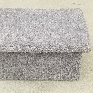 May include: A rectangular footstool covered in a thick, light gray shag carpet material. The piece features a flat, overhanging top surface and a solid, box-like base, all uniformly upholstered in the same textured, fuzzy gray fabric throughout.