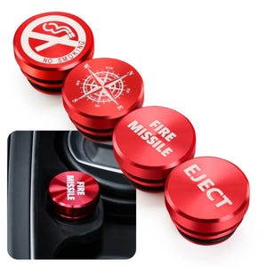 May include: A set of four circular red car cigarette lighter plug covers. Three are displayed separately, featuring white graphics: a no smoking symbol, a compass rose, and the text Fire Missile and Eject. One is installed in a car console.