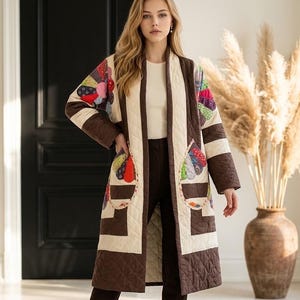 May include: A long, quilted coat featuring a cream and dark brown geometric pattern. The coat includes colorful, fan-shaped patchwork appliqués on the sleeves and pockets. It is worn over a plain cream top and dark brown trousers with dark brown boots.