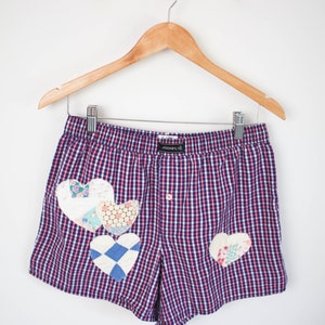 Pode incluir: Boxer de xadrez azul e vermelho com um design de coração de patchwork. Os shorts têm um fecho de botão e uma cintura elástica. A marca "JOCKEY" é visível na cintura.