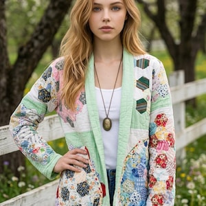 May include: A long-sleeved quilted jacket featuring a patchwork design of multicolored hexagonal fabric pieces. The jacket has a light green trim along the front opening and cuffs, two large rounded pockets, and is worn over a plain white top.