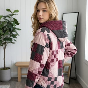 May include: A hooded jacket featuring a patchwork design with alternating squares of light pink, dark charcoal grey, and deep burgundy floral fabric. The garment has long sleeves, a hood, and a curved hemline, constructed with visible quilted stitching.