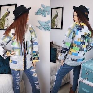 May include: A grey and white patchwork jacket with a blue, green and yellow pattern. The jacket is worn over a black shirt and blue jeans. The model is wearing a black hat.