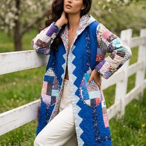 May include: A long-sleeved quilted coat featuring a vibrant blue base with a zigzag edge pattern. The garment incorporates patchwork fabric panels with various floral and geometric prints on the sleeves, hood, and two large rounded front pockets.