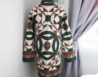 Puede incluir: Un abrigo de manga larga confeccionado en tela acolchada con un diseño de patchwork. La prenda muestra un patrón repetitivo de segmentos de tela en verde oscuro, crema y estampados florales dispuestos en formas geométricas y circulares.