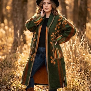 May include: A long, forest green open-front coat featuring a shawl collar, two large patch pockets, and a repeating orange and brown leaf pattern. The coat is worn over a black shirt, blue jeans, and brown leather boots, paired with a black hat.