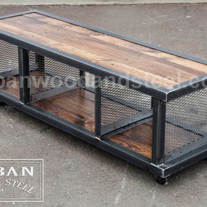 May include: A rustic industrial coffee table with a wooden top and metal frame. The table has three open shelves with wire mesh sides. The table is on wheels and has a black metal finish.