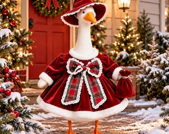 May include: A white goose figurine wearing a deep red velvet dress with white faux fur trim, a matching wide-brimmed hat, and a large red and green plaid bow. The goose holds a small red velvet drawstring pouch in its wing.
