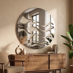 May include: A large circular wall mirror featuring a decorative overlay of layered, wave-like cutouts across the glass surface. The mirror reflects the surrounding room, creating a multi-dimensional effect with its abstract, flowing horizontal lines.