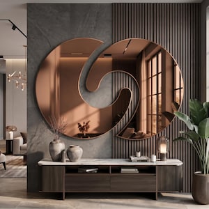 May include: A large, circular, copper-tinted wall mirror featuring a central, swirling, abstract cutout design. The mirror is mounted on a wall with a combination of dark gray stone tiles and vertical brown wooden slats, positioned above a console.