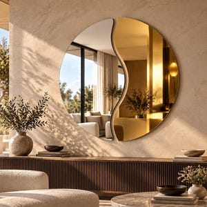 May include: A large circular wall mirror featuring a split design with one half in clear glass and the other half in a reflective gold finish. The mirror has a curved, wave-like dividing line that separates the two distinct reflective surfaces.
