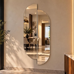 May include: A wall-mounted mirror featuring two offset semi-circular panels with thin metallic frames. The design creates a split, elongated shape that reflects a dining room interior, including chairs, a table, and a pendant light fixture.