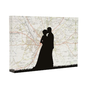 May include: A rectangular canvas print featuring a black silhouette of two figures standing together against a detailed map background of York, England. The bottom edge of the canvas displays a black graphic of grass blades across the entire width.
