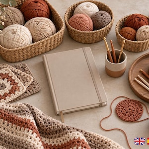 May include: A beige notebook sits among crochet supplies including yarn balls in woven baskets, a striped crochet blanket, granny squares, a circular coaster, a ceramic cup with crochet hooks, and a wooden tray with scissors and stitch markers.